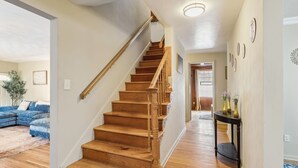 Eine Holztreppe mit Handlauf, die zu einer zweiten Etage führt. Im Vordergrund befindet sich ein blaues Ecksofa und auf der rechten Seite ein kleiner Tisch mit Vasen.