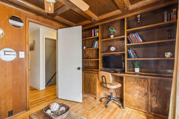 A wooden interior with a desk, chair, bookshelves, and a television.