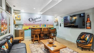Una sala de estar con una zona de bar, un sofá, una mesa de centro y un televisor montado en la pared.