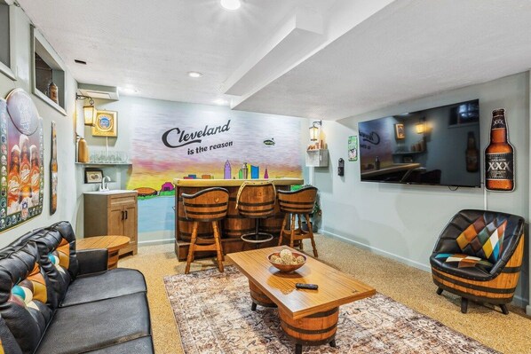 A living room with a bar area, a sofa, a coffee table, and a TV mounted on the wall.