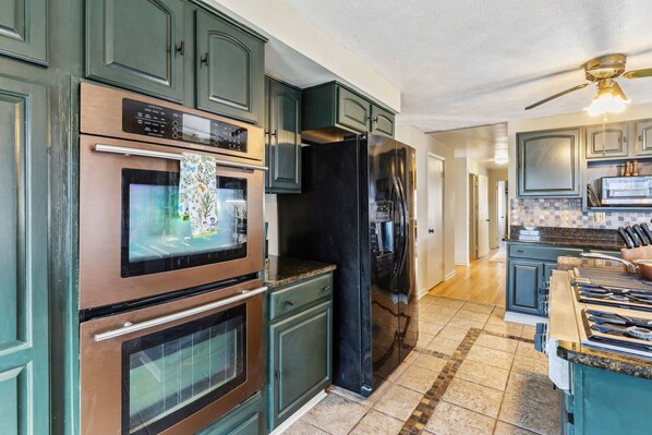 Una cocina con armarios verde oscuro, electrodomésticos de acero inoxidable y piso de baldosas.