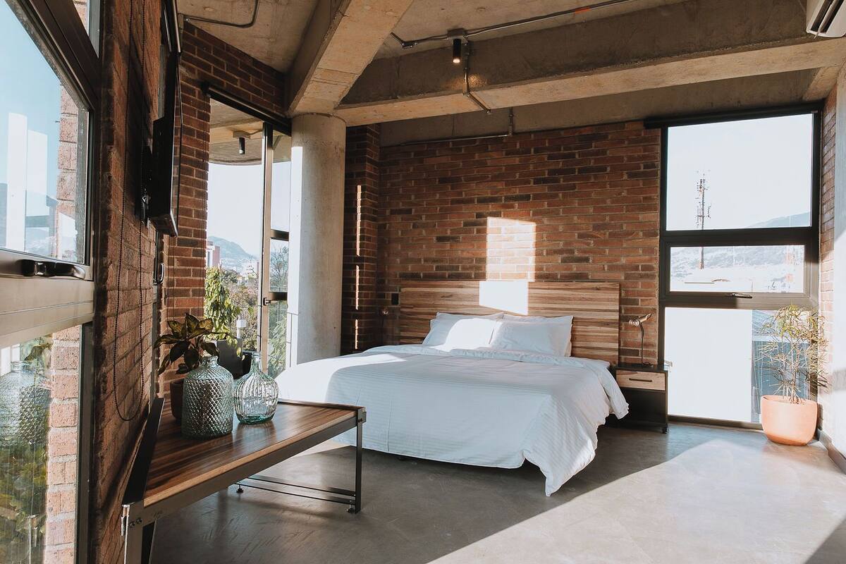 A modern bedroom with a brick wall, a large window, and a bed with white linens.