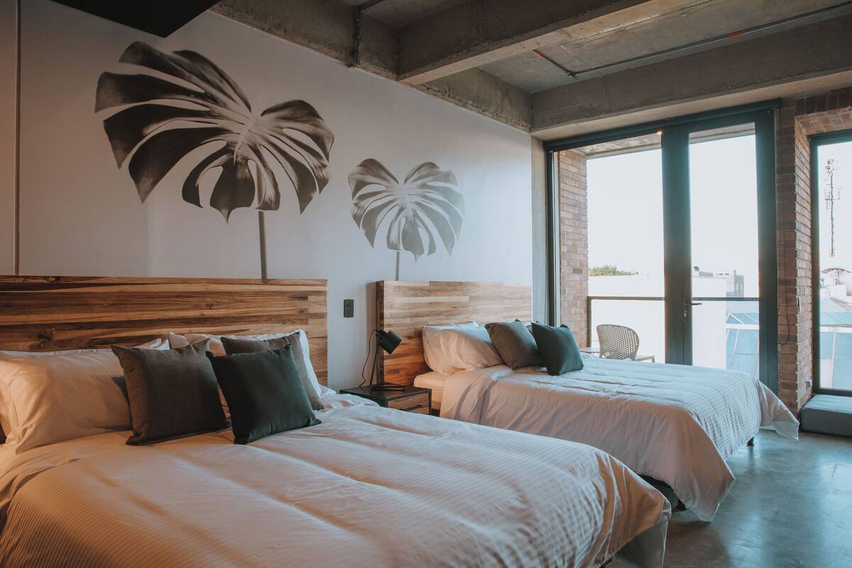 A hotel room with two beds, a wooden headboard, a large window, and a view of the city.