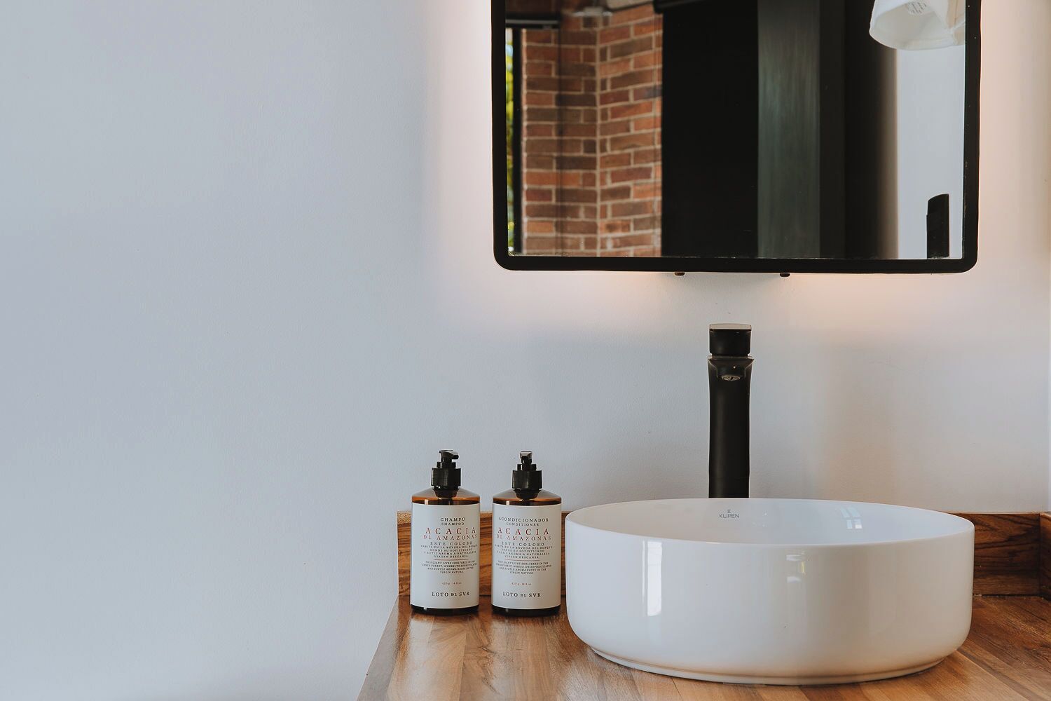 A bathroom with a white sink, two bottles of shampoo, and a mirror.