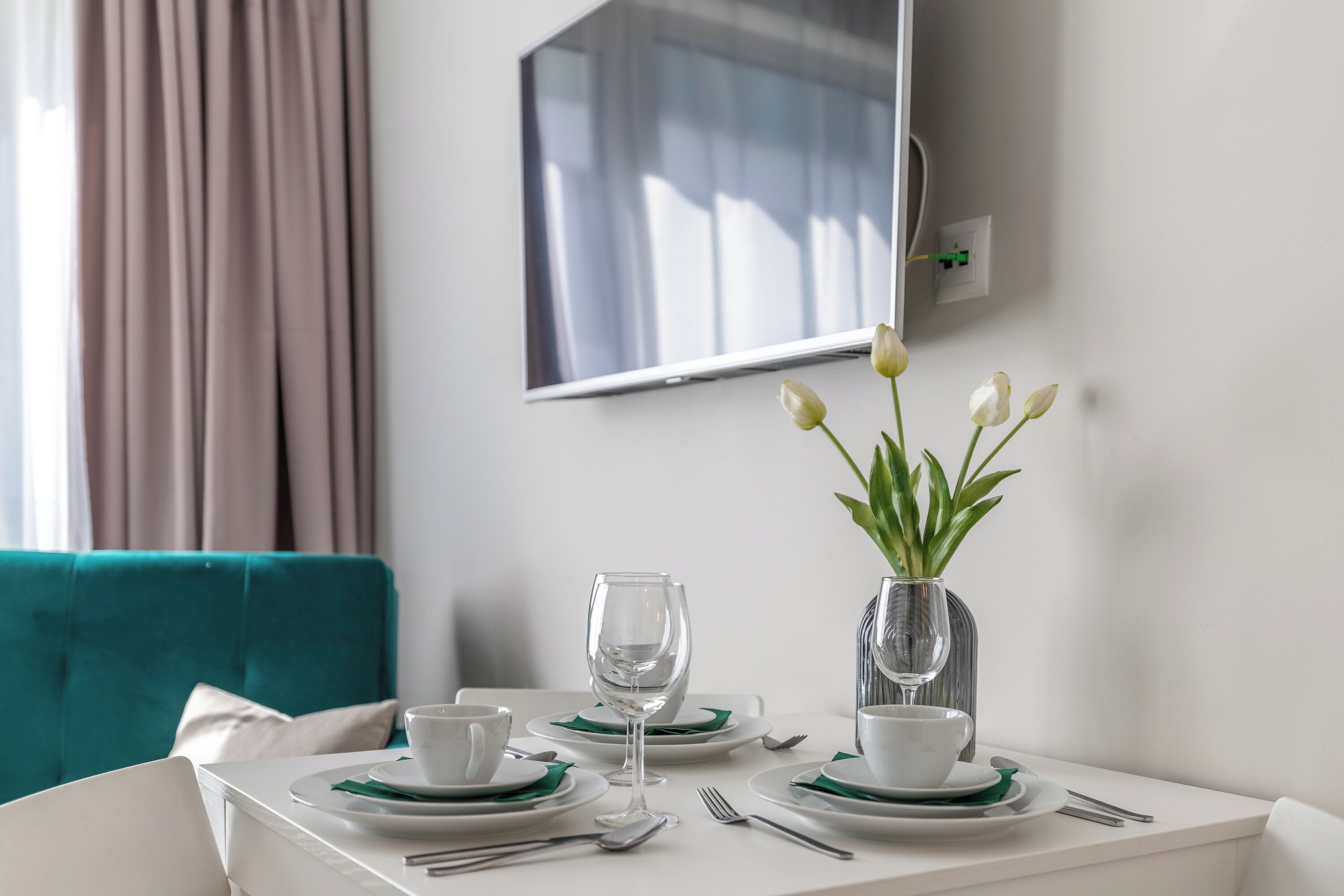 A neatly set dining table with white plates, green napkins, and a vase with white flowers.
