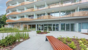 Un immeuble moderne à plusieurs étages, doté de balcons, d’une cour intérieure avec un banc et d’une entrée en verre.