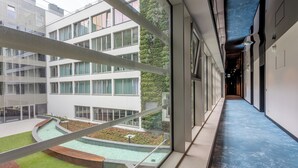 Un bâtiment moderne doté de grandes fenêtres, d’une cour agrémentée d’un élément décoratif aquatique et d’un plafond bleu.