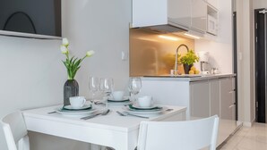 Une cuisine moderne avec des meubles blancs, une table à manger dressée avec de l’assiette blanche et des serviettes vertes, et un vase rempli de fleurs blanches.