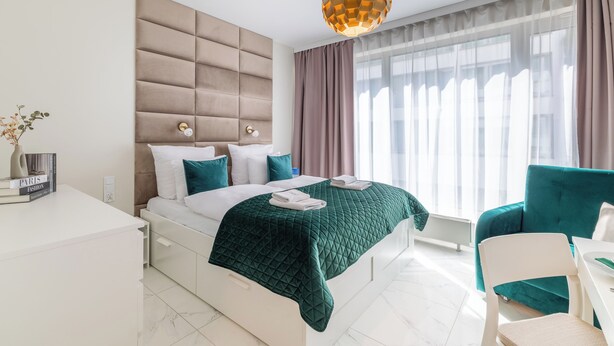 Une chambre d’hôtel moderne, dotée d’un grand lit, d’une table de chevet, d’une chaise et offrant une vue sur la ville grâce à de grandes fenêtres.