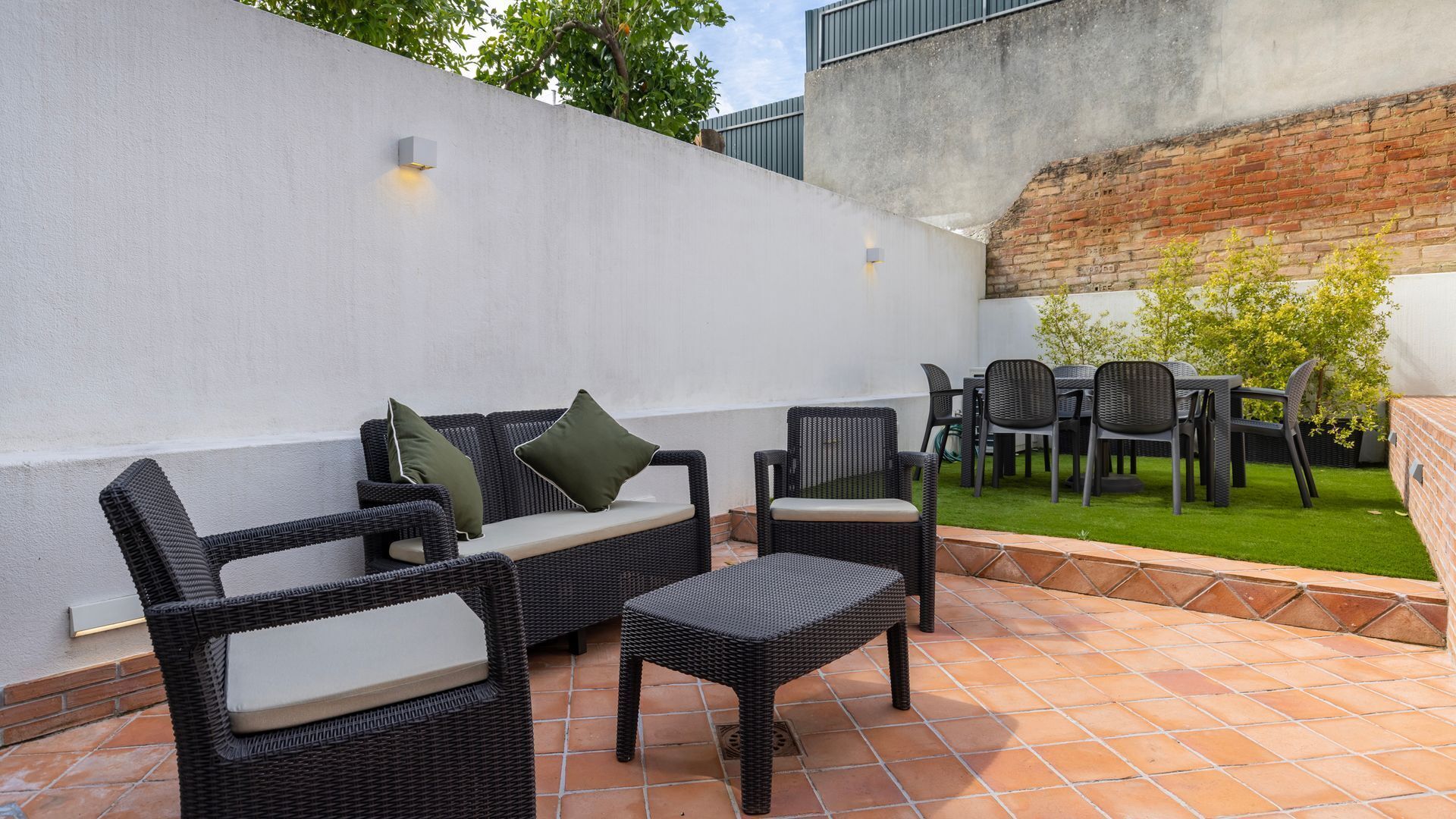 An outdoor patio with wicker furniture, a brick wall, and a grassy area.