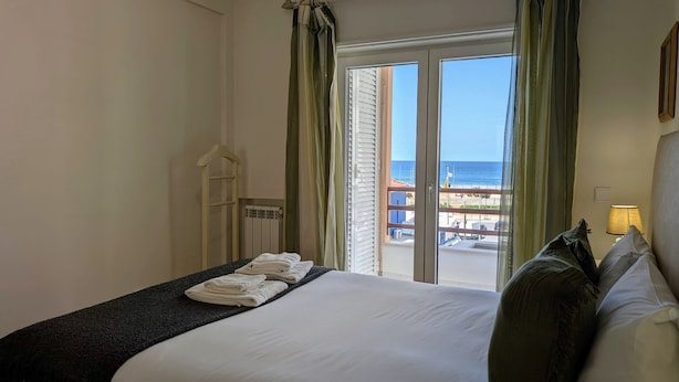 A hotel room with a bed, a window with a view of the beach, and a balcony with a railing.