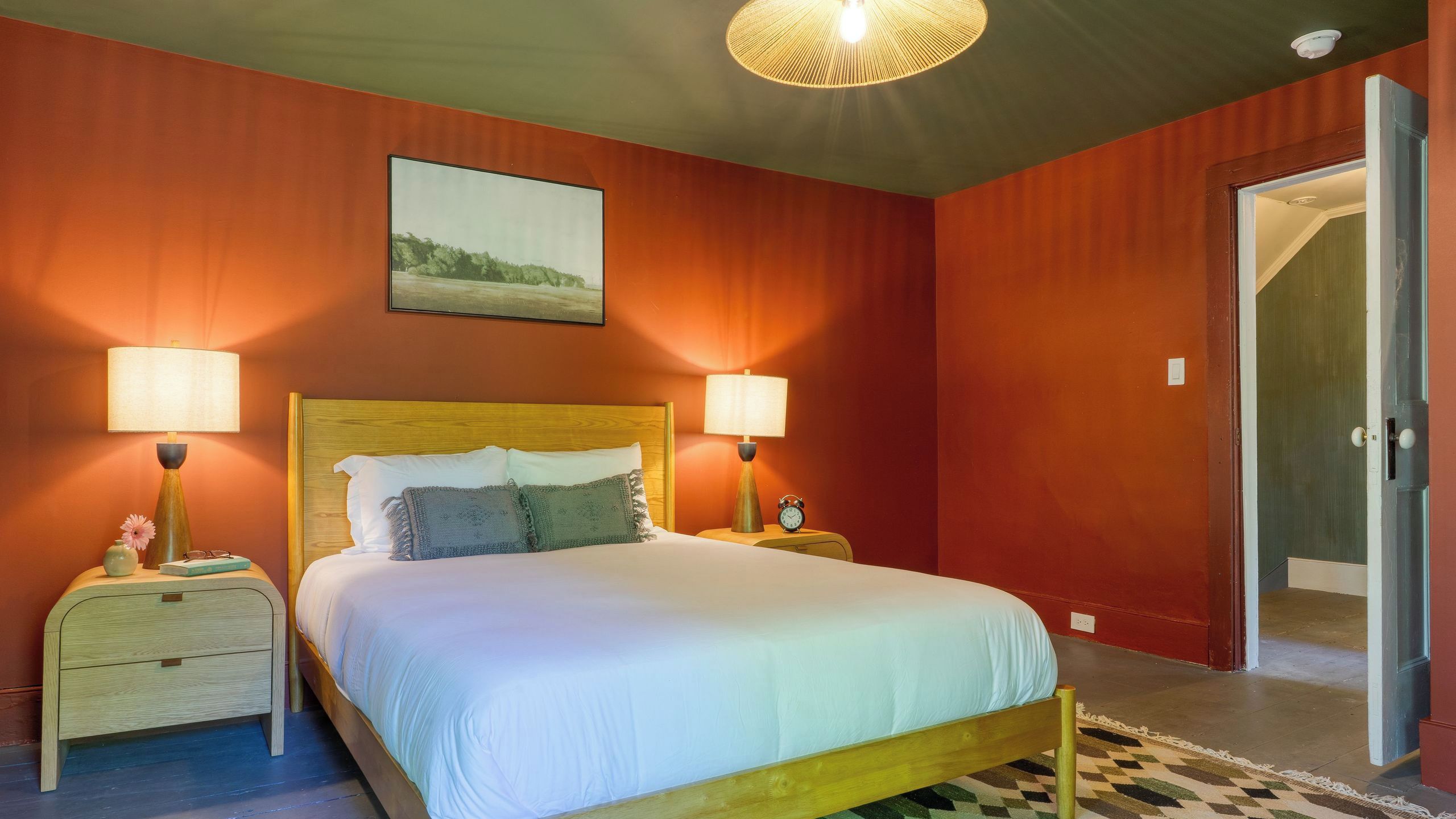 A bedroom with a bed, two bedside tables, a nightstand, a lamp, a clock, and a door.