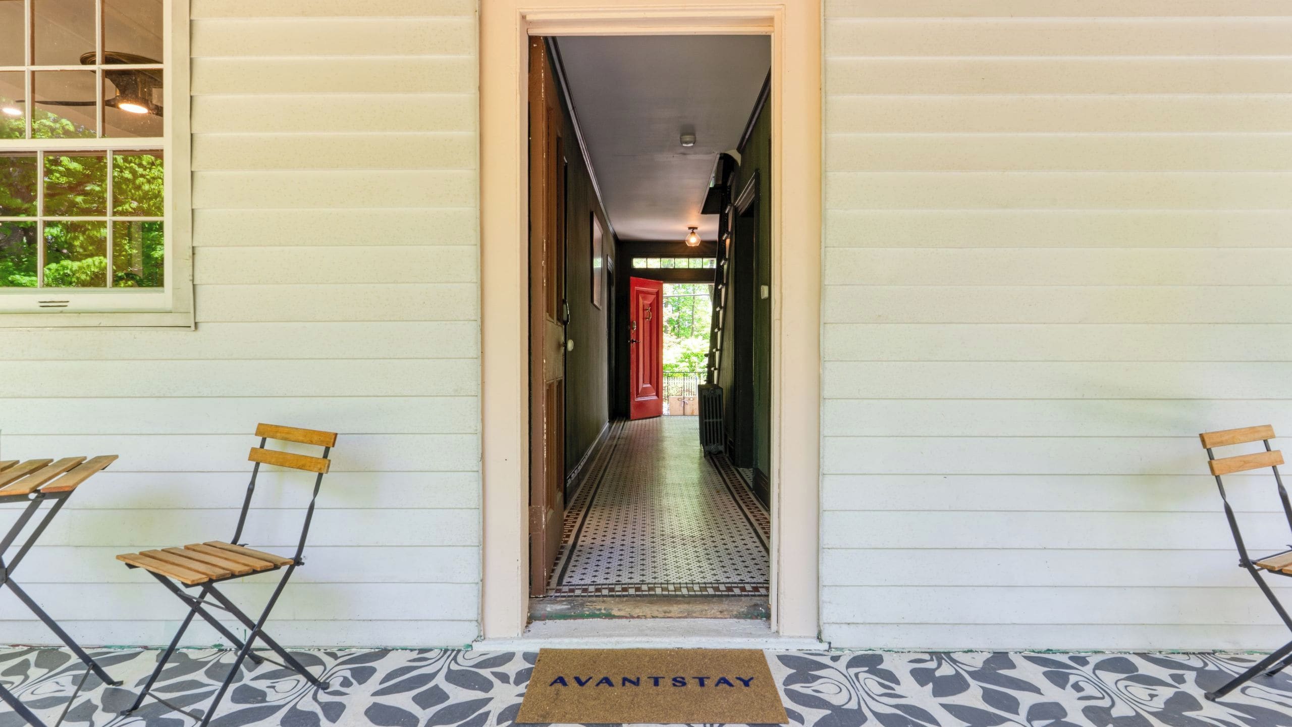 A narrow hallway with a red door, two folding chairs, and a doormat with 'AVANTSTAY' text.