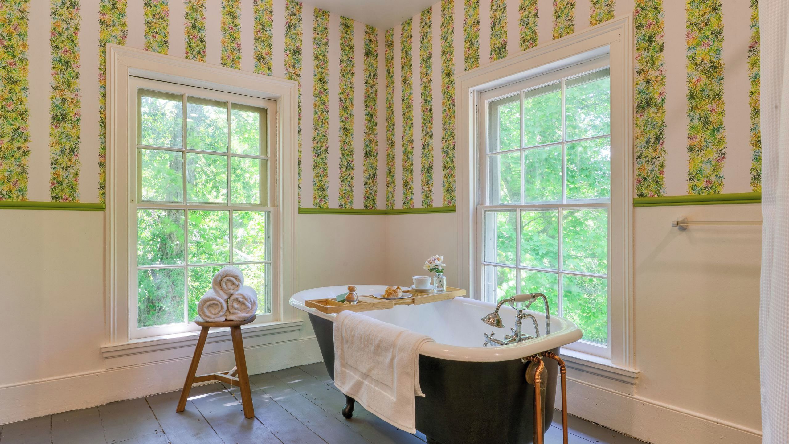A bathroom with a freestanding bathtub, two windows, and a wooden stool.