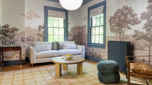 A room with a sofa, a round wooden table, a green armchair, and a radiator. - Relax in Style at Historic Modern on Main With Modern Amenities & Wooded Views (Stone Ridge)