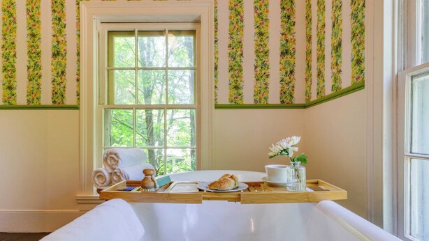 A bathroom with a bathtub, a window, and a wooden tray with towels and toiletries. - Relax in Style at Historic Modern on Main With Modern Amenities & Wooded Views (Stone Ridge)