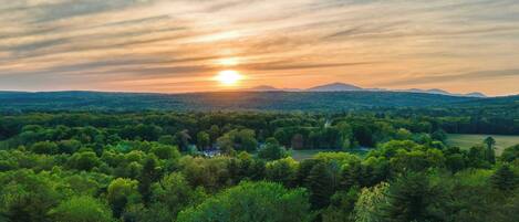 A landscape with a sunset over a forested area and distant mountains.