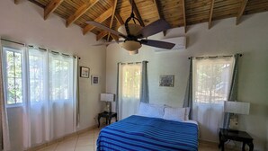 Une chambre à coucher avec un lit, un ventilateur de plafond et une fenêtre avec des rideaux.