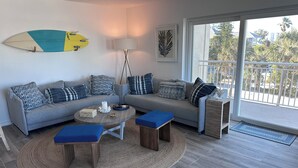 Una sala de estar moderna con un sofá gris, cojines azules, una mesa de centro redonda y una tabla de surf en la pared.