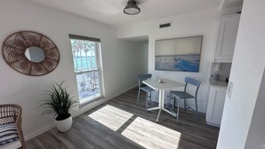 Una cocina moderna con armarios blancos, una mesa de comedor con sillas, un ventanal con vistas a palmeras y un espejo decorativo en la pared.