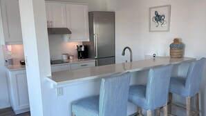 Una cocina moderna con una isla central, taburetes de bar y un refrigerador de acero inoxidable.