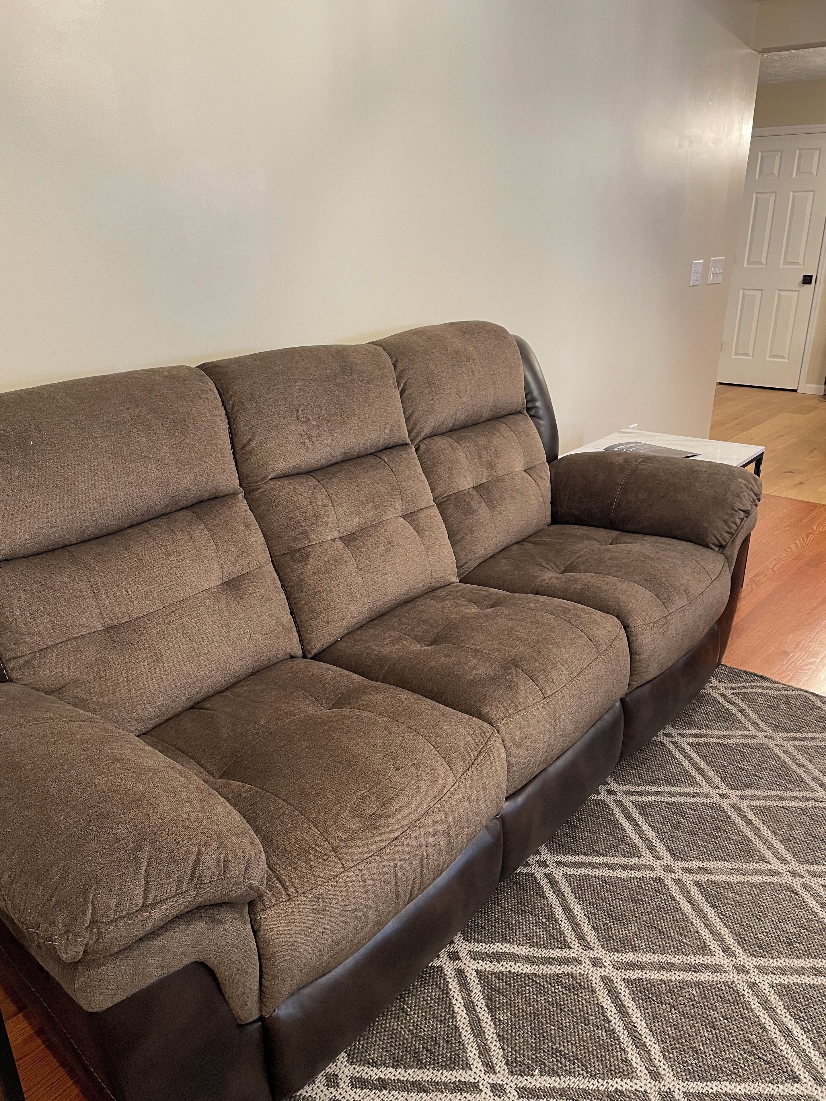 A brown sofa with a dark frame in a room with wooden flooring and a patterned rug.