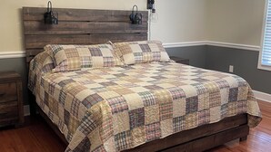 Une chambre à coucher avec un lit en bois, une courtepointe, deux lampes fixées au mur et un luminaire au plafond.