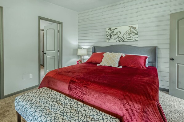 A bedroom with a large bed, a bedside table with a lamp, and a door leading to another room. - Southgate: 800 Yards to Campus/Kyle Field (College Station)