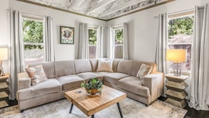 A living room with a beige sectional sofa, a wooden coffee table with a plant, and a framed picture on the wall.