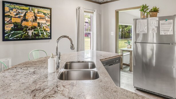 A kitchen with a marble countertop, stainless steel sink, and a refrigerator.
