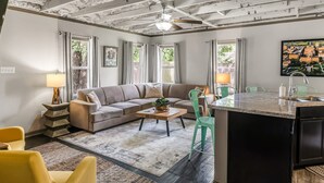 A living room with a sofa, coffee table, and a kitchen area with a sink and chairs.