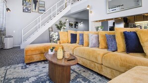 A modern living room with a large sofa, a coffee table, and a staircase. - Downtown Penthouse #5 | Vintage +gym & balcony (Chicago)