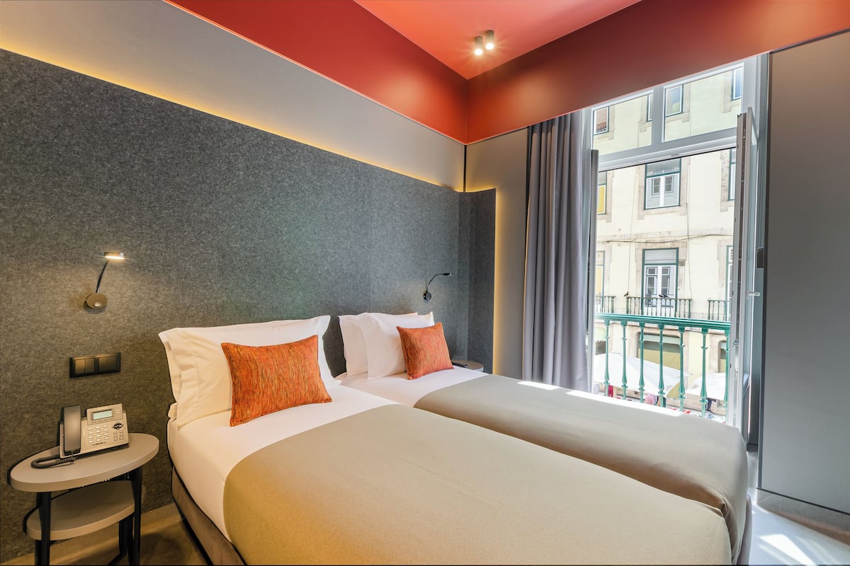 Une chambre d’hôtel avec deux lits, un téléphone sur une table de chevet et une vue sur un immeuble par la fenêtre.
