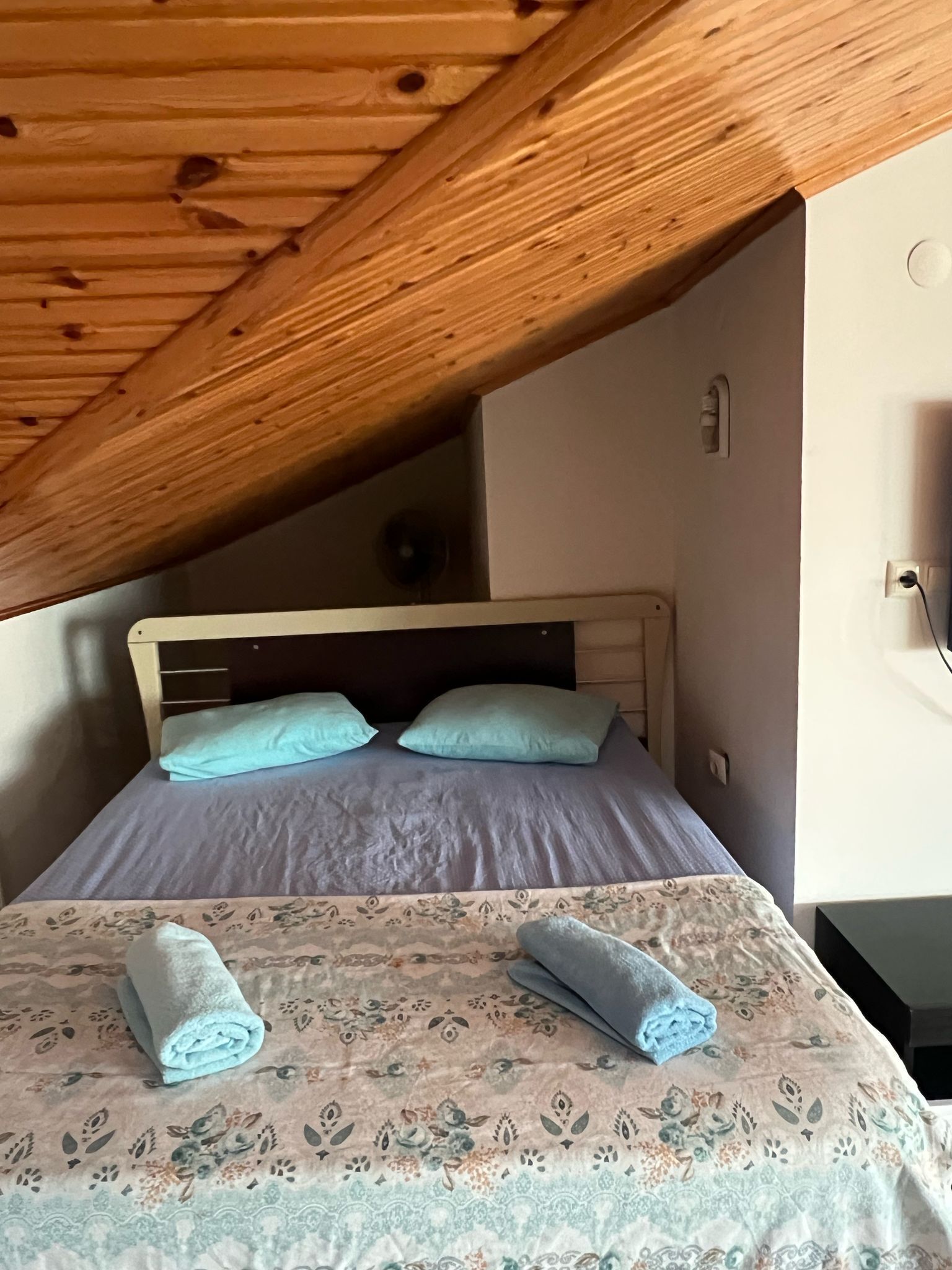 A bedroom with a wooden ceiling, a bed with two pillows, and a floral-patterned bedspread.