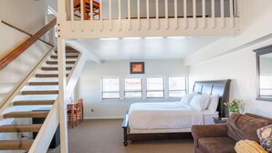 Ein Schlafzimmer mit Etagenbett, einer Holztreppe, einer Couch und einem Fenster mit Jalousien.