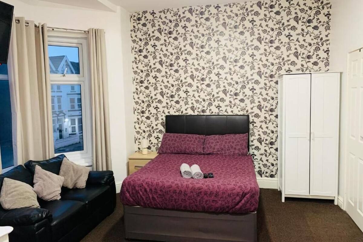 A bedroom with a bed, a sofa, a wardrobe, and a window with curtains.