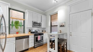 A modern kitchen with white cabinets, a microwave, a stove, and a dishwasher. There is a window with blinds and a small plant on the counter.