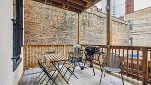 A covered outdoor patio with a brick wall, wooden furniture, and a grill.
