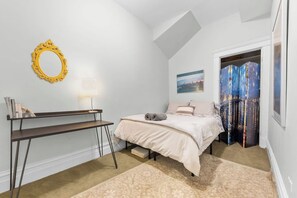 A bedroom with a bed, a desk, a lamp, a mirror, and a window with curtains. - Secret Gallery on the Park - 2bd/1ba (Chicago)