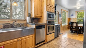 A kitchen with wooden cabinets, stainless steel appliances, a granite countertop, and a dining area with a table and chairs. - Lakeside Haven, a cozy and relaxing home that sleeps 24 with pool/hottub access! (Garden City)