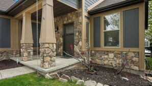 A house with a stone facade, a porch with a swing, and a small garden with rocks and plants. - Lakeside Haven, a cozy and relaxing home that sleeps 24 with pool/hottub access! (Garden City)