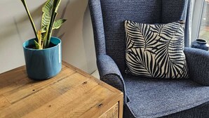 Una esquina de una habitación con un sillón azul, una mesita de madera y una planta en maceta.