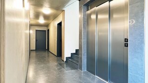 A modern hallway with a marble floor, a staircase, and a wall-mounted elevator. - Luxurious 4-room penthouse, roof terrace, parking space, e-charging station (Wachtberg)