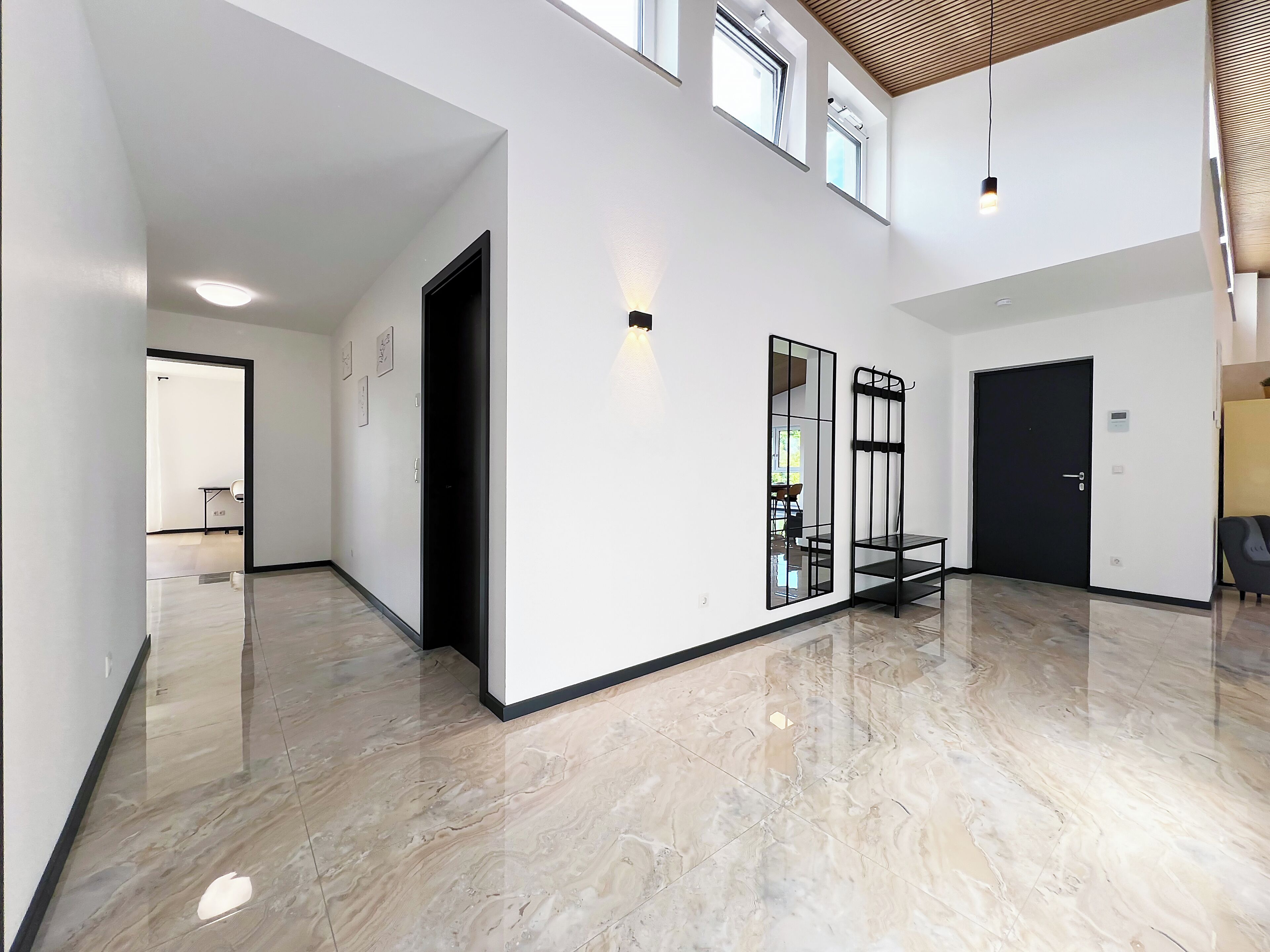 A spacious hallway with a polished marble floor, a black-framed mirror, and a black door.