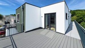 A modern building with a flat roof, large sliding glass door, and a balcony with a metal railing. - Luxurious 4-room penthouse, roof terrace, parking space, e-charging station (Wachtberg)