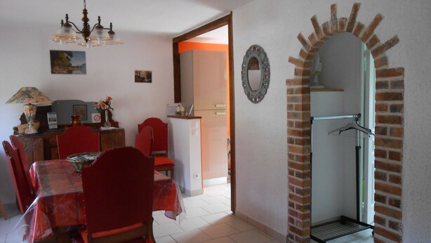 Un coin repas avec une table, des chaises et un lustre. On y trouve également un réfrigérateur et un miroir accroché au mur.
