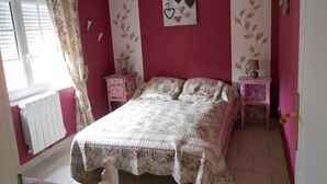 Une chambre à coucher avec un lit, deux tables de chevet, un radiateur et une fenêtre avec des rideaux.