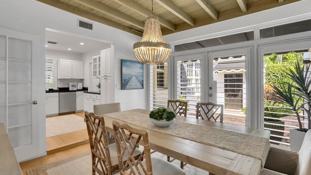 A dining area with a wooden table, chairs, and a chandelier. There is a view of the outside through large windows. - 2 Side-by-Side Delray Beach Homes & Guest House - 1 blk to beach & Atlantic Ave! (Delray Beach)