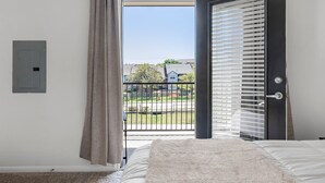 Ein Schlafzimmer mit großem Fenster, einer Tür mit Jalousien und Blick auf eine Wohngegend.