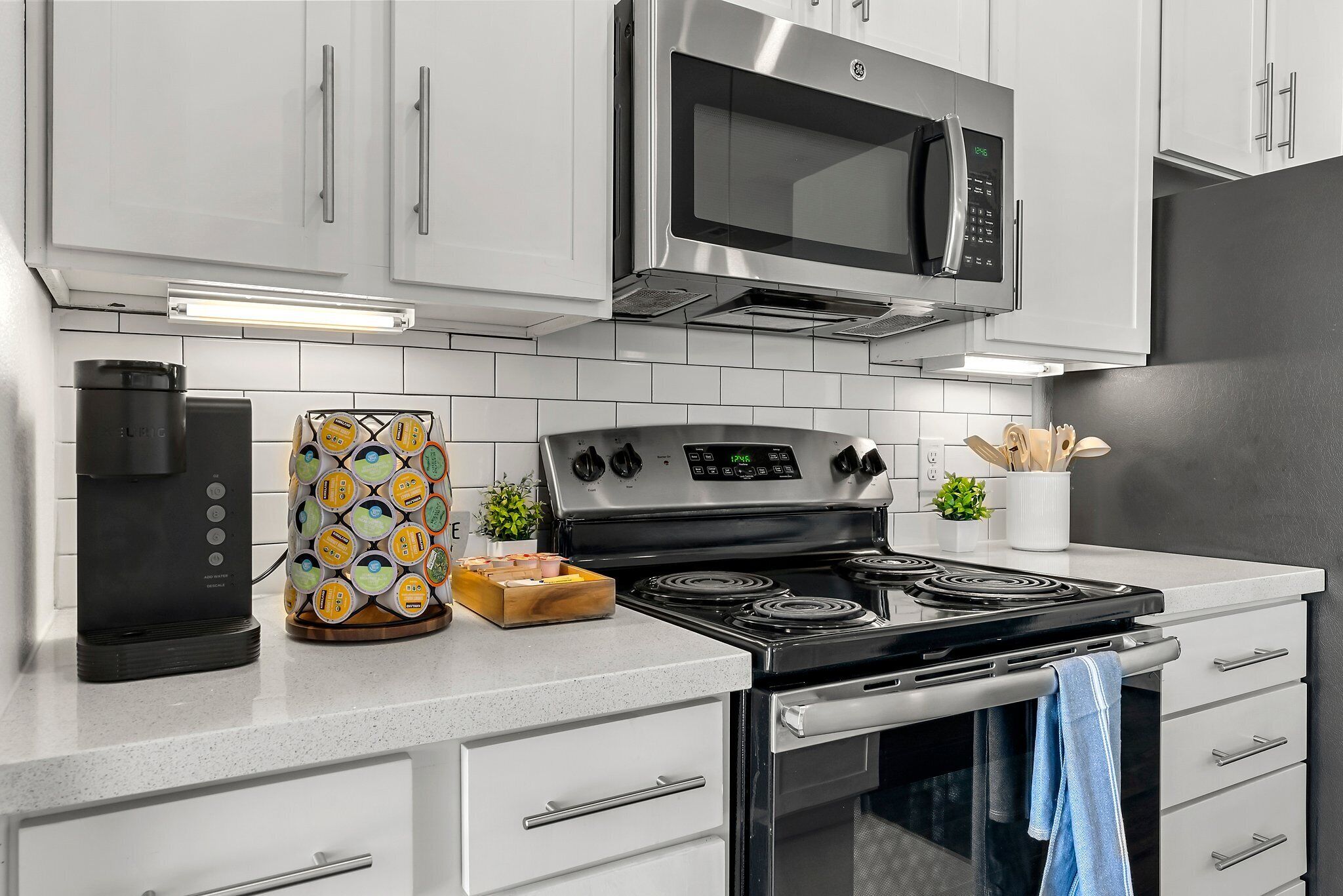 A modern kitchen with white cabinetry, a stainless steel microwave, a coffee maker, a decorative container, and a stove.